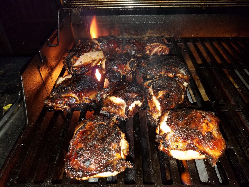 Chicken thighs finishing on the propane grill, flame visible