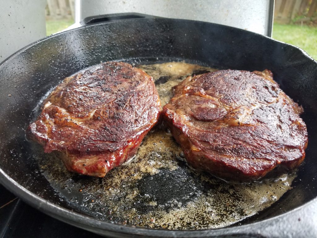 Ribeyes searing in the cast iron pan