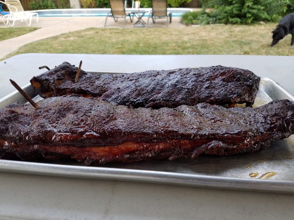 Entire hanging rack of ribs lowered onto a sheet pan to remove from the smoker