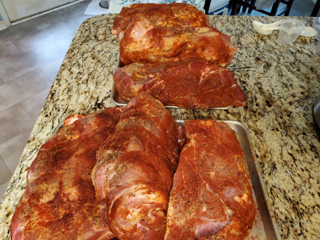 Seasoned raw pork butts on sheet pans on a granite counter