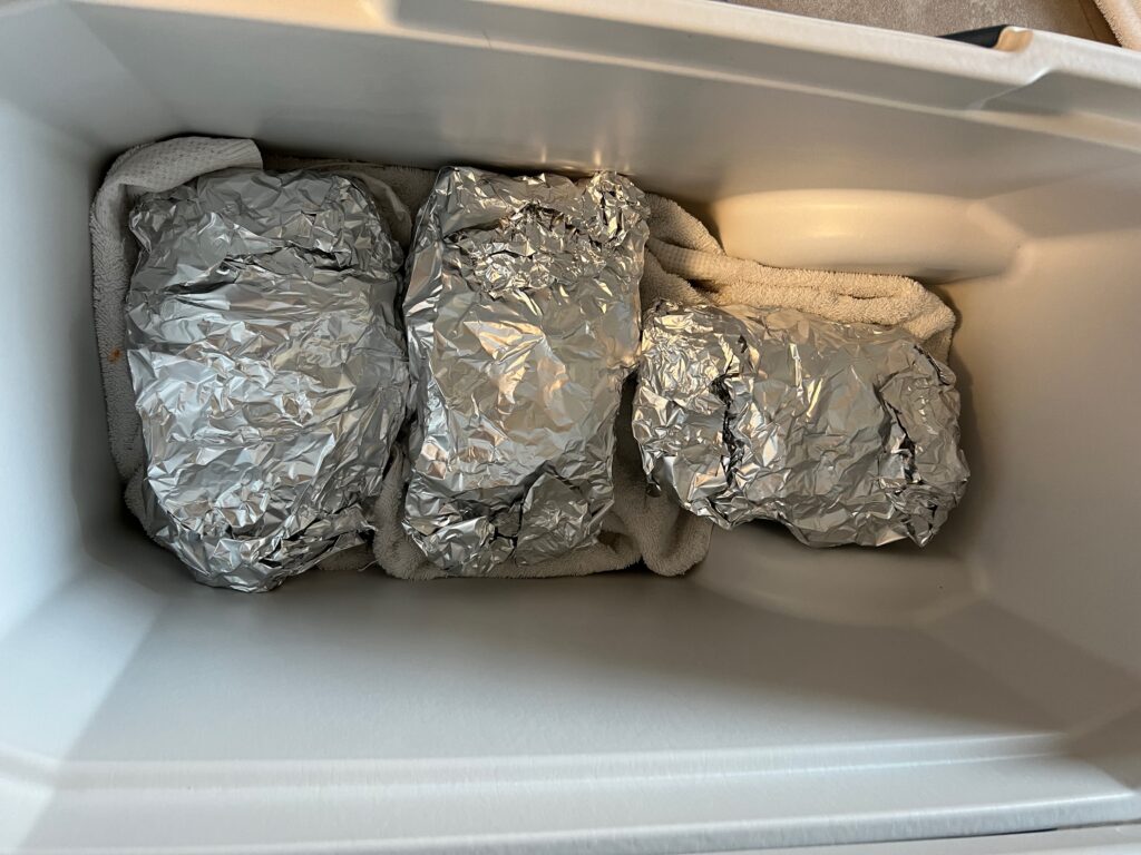 Foil-wrapped pork butts resting in a cooler