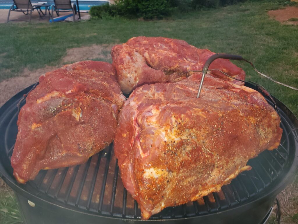 Seasoned raw pork butts on the smoker grate at the start of a cook
