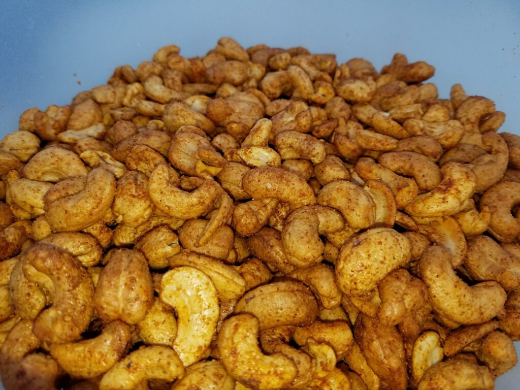 Close-up of finished spice-coated smoked cashews piled in a light blue bowl