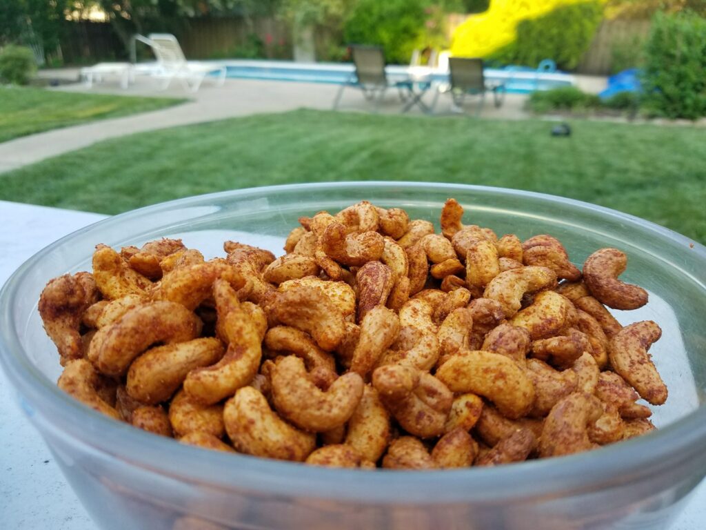 Finished smoked nuts: hickory smoked cashews in a clear glass bowl, backyard lawn and pool in the background