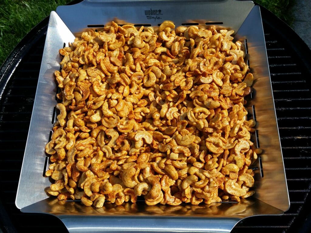 Seasoned cashews spread in a Weber Style slotted grill pan on a grill grate at the start of the cook